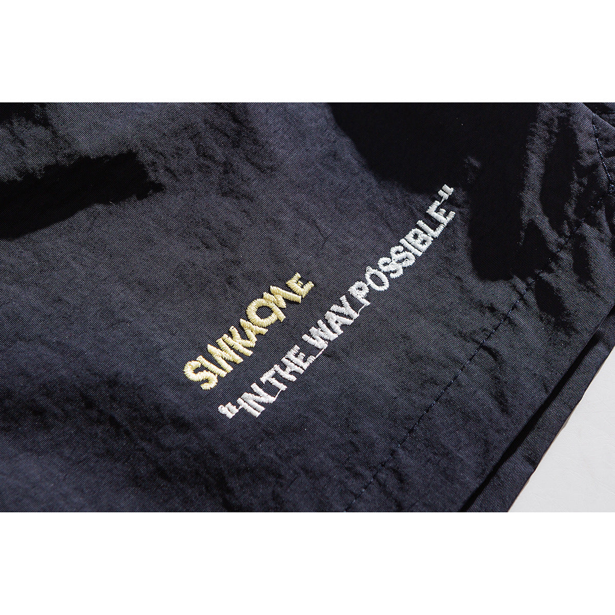 Close-up of dark shorts with yellow and white embroidered lettering on the fabric.