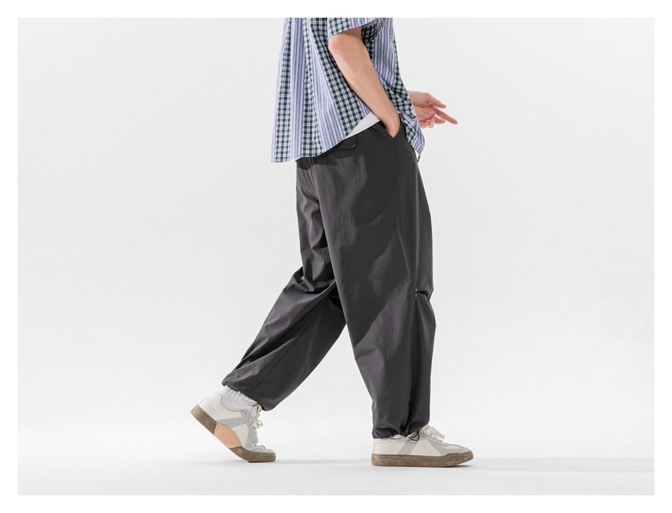 Side and rear view of a cropped model walking in loose charcoal-gray trousers with gathered hems.