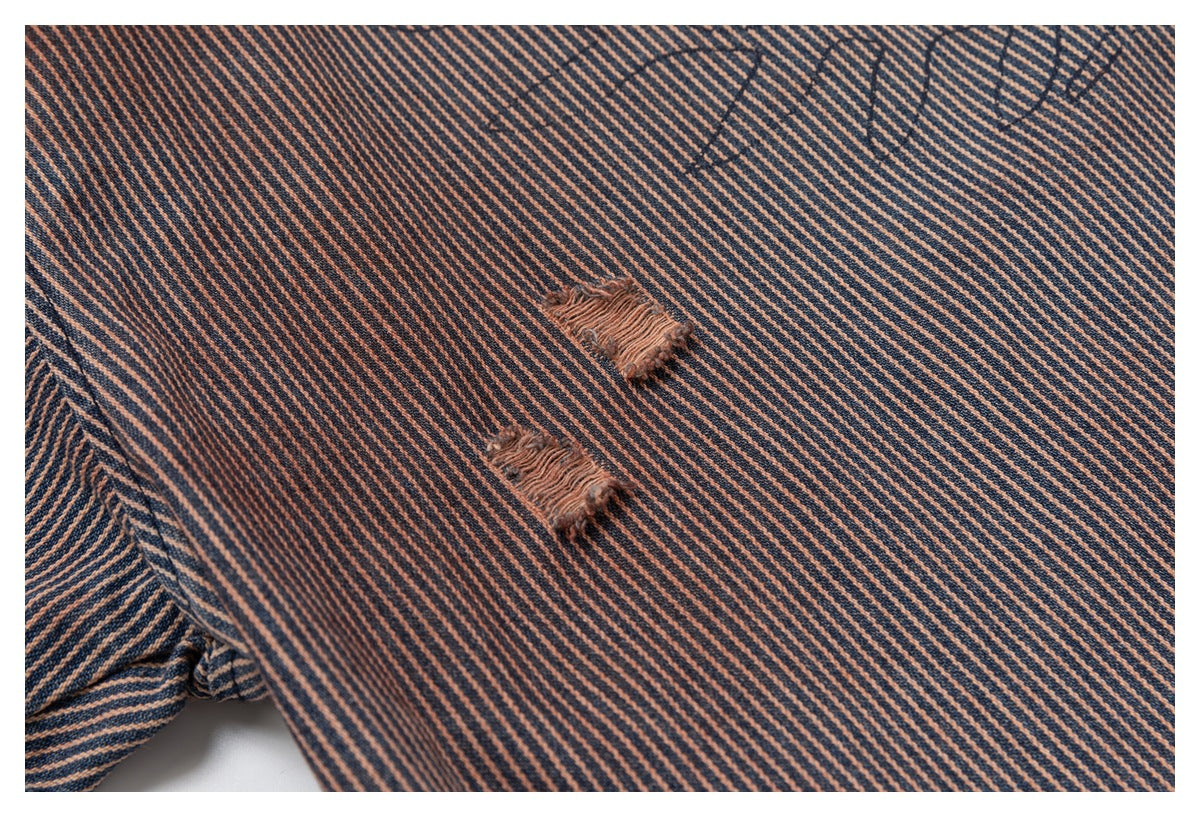 Close-up of two distressed, frayed patches on navy and rust diagonal-striped shirt fabric.