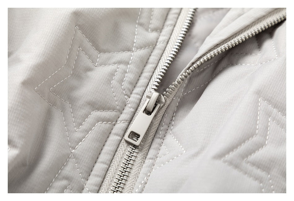Close-up of a light gray quilted jacket's metal zipper and stitched star pattern.