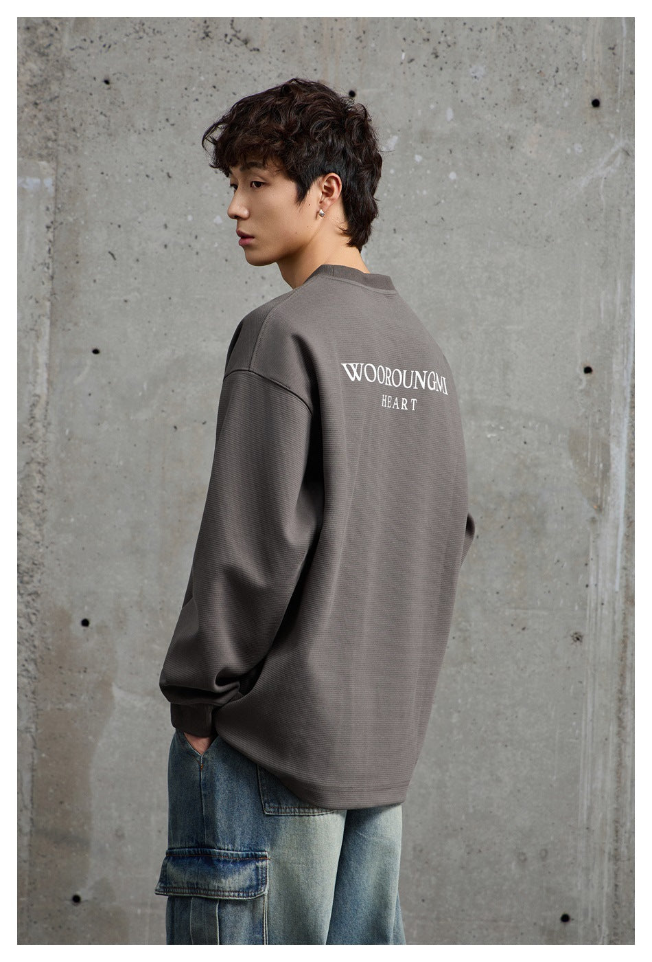 Model showing the back of a charcoal-gray oversized top with white “WOOROUNGMI HEART” lettering.