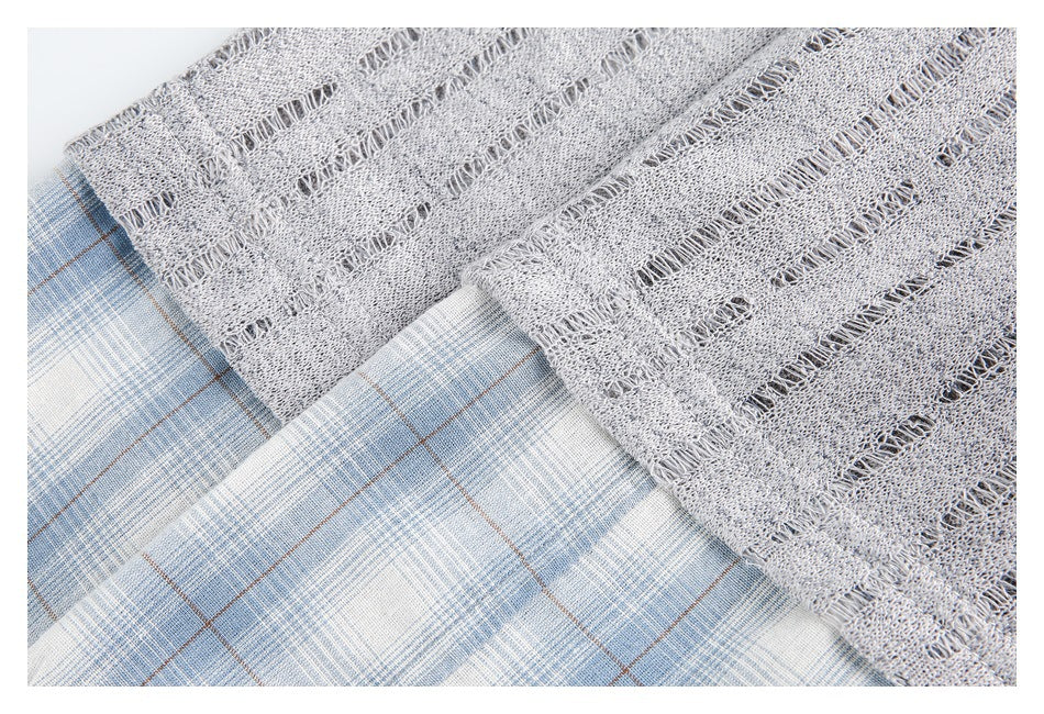 Close-up of a blue plaid inset beneath the gray openwork fabric of a top.