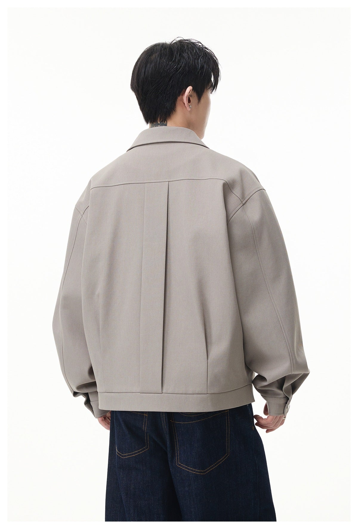 Back view of a model wearing a light taupe jacket with a center back pleat and wide hem band.
