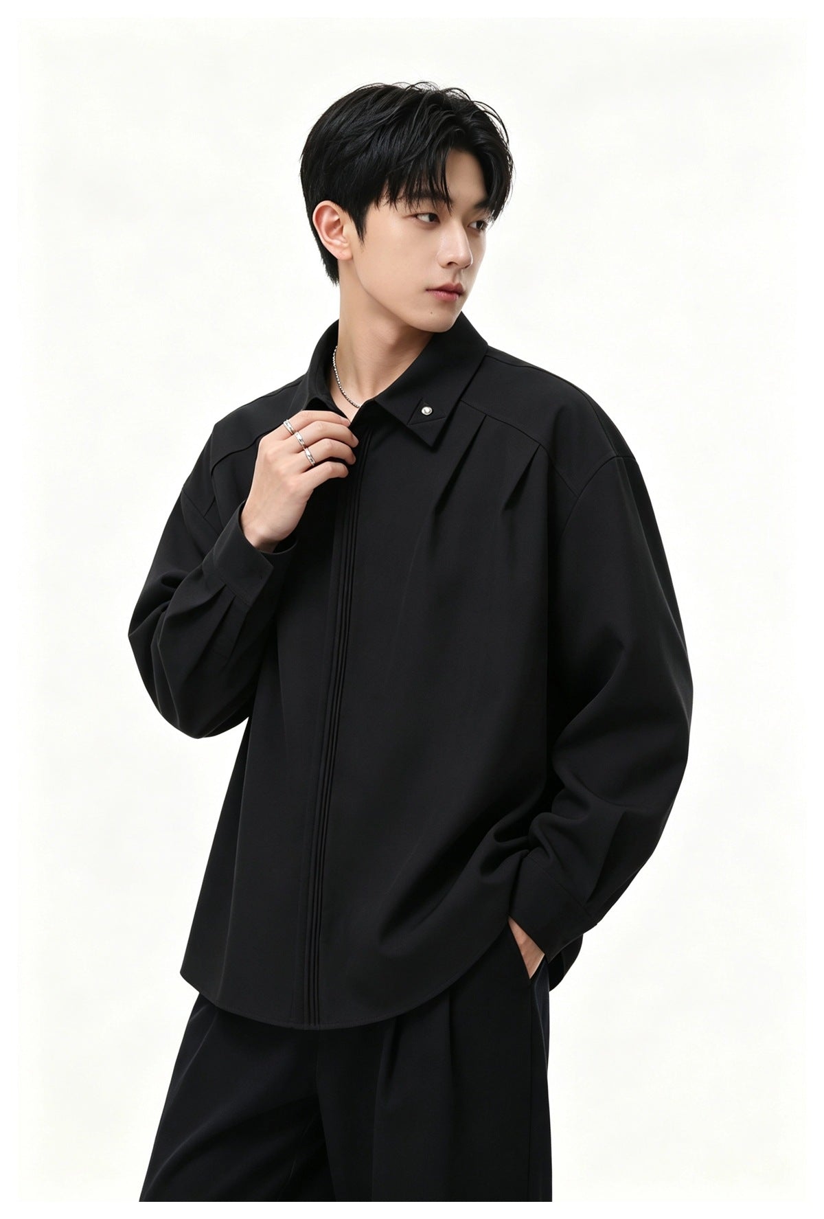 Model wearing a black long-sleeve shirt with a studded collar point and pintuck placket, with black trousers