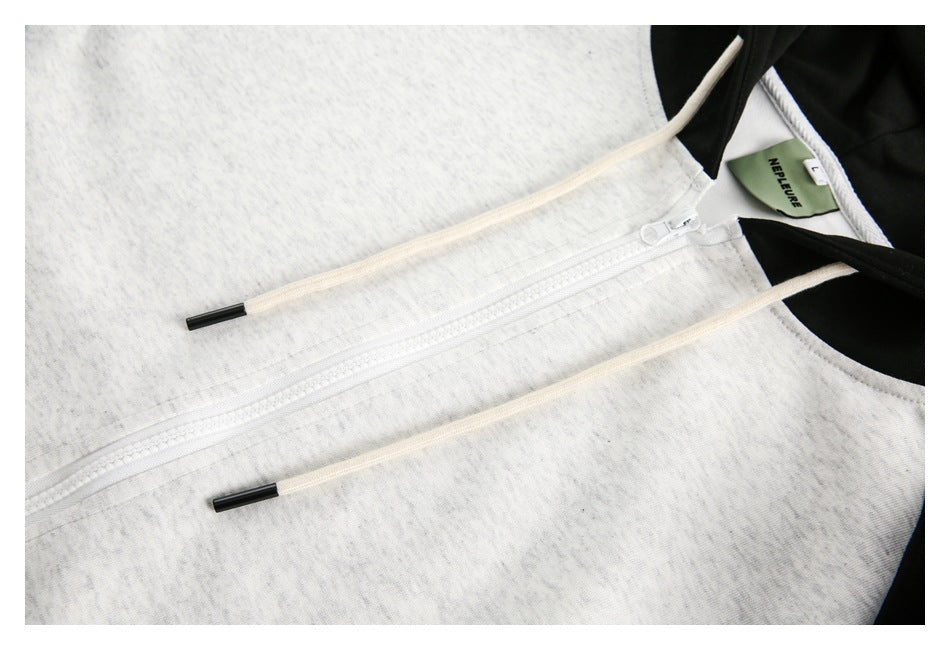 Close-up of a light gray hoodie’s front zipper and cream drawstrings, with black hood trim at the neckline.