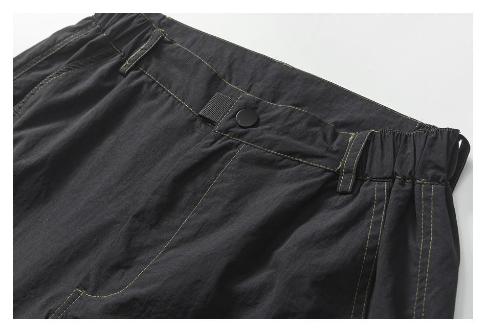 Close-up of the charcoal shorts' buttoned waistband, belt loops, elastic side panel, and contrast stitching.