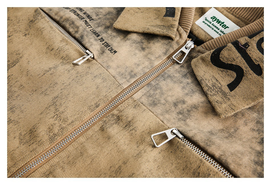Close-up of the tan mottled jacket front with multiple silver zippers and a wide collar bearing black lettering.