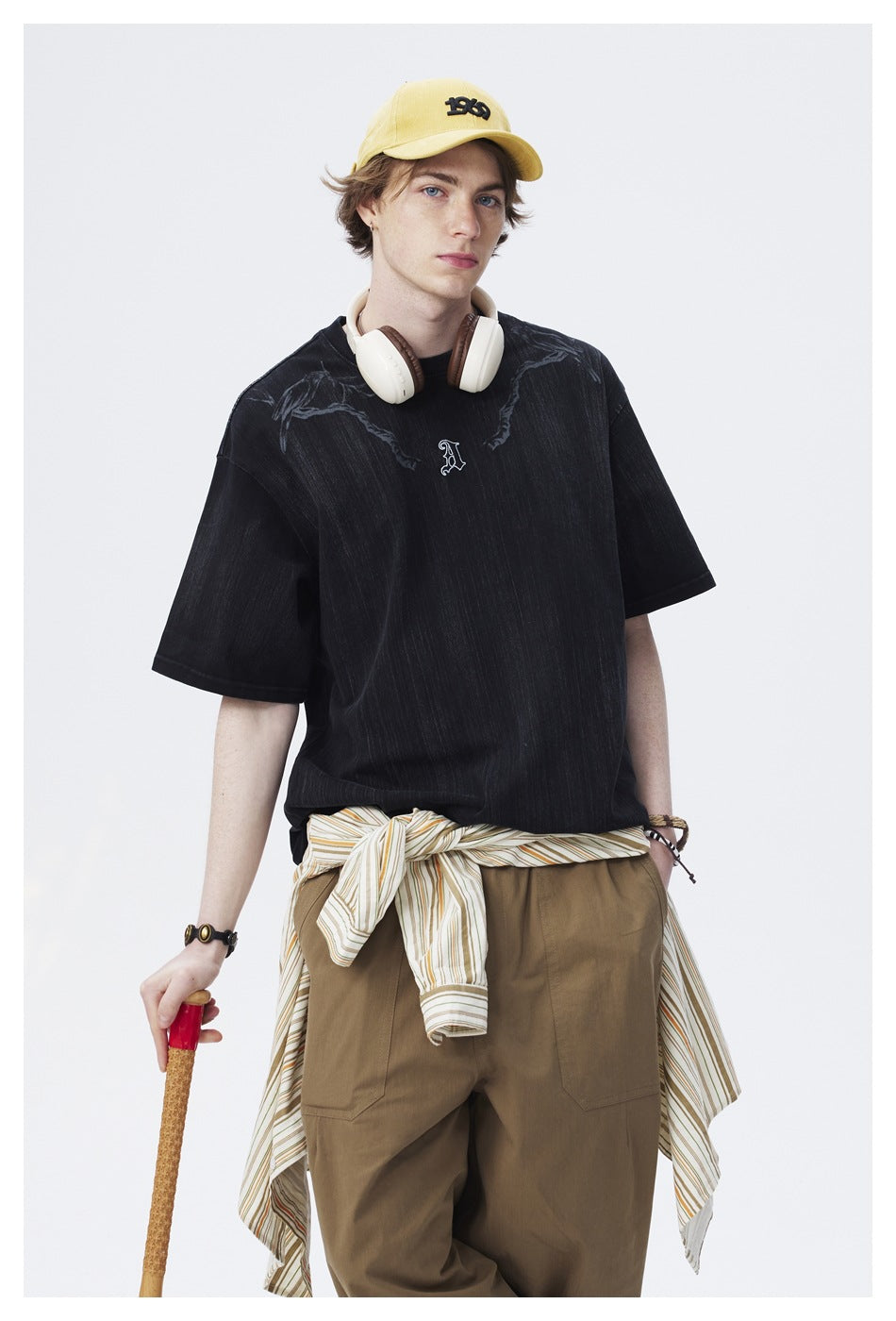 Closer view of a model wearing an oversized black T-shirt with dark shoulder graphics and a small embroidered chest letter.