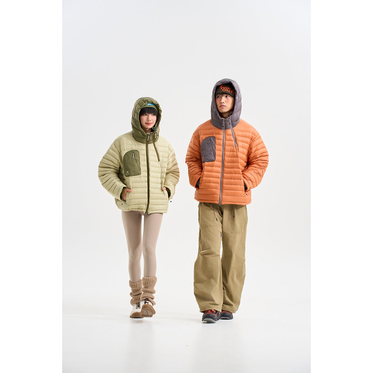 Two models wearing hooded quilted jackets: pale sage with olive accents and orange with gray accents.