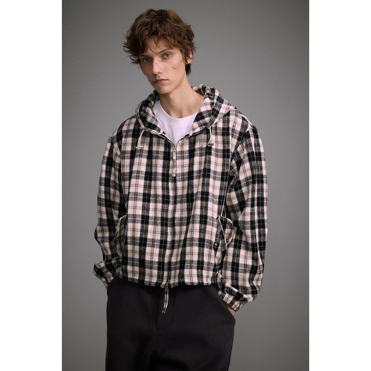 Model wearing a cream and black plaid hooded zip jacket with drawstrings and front pockets.