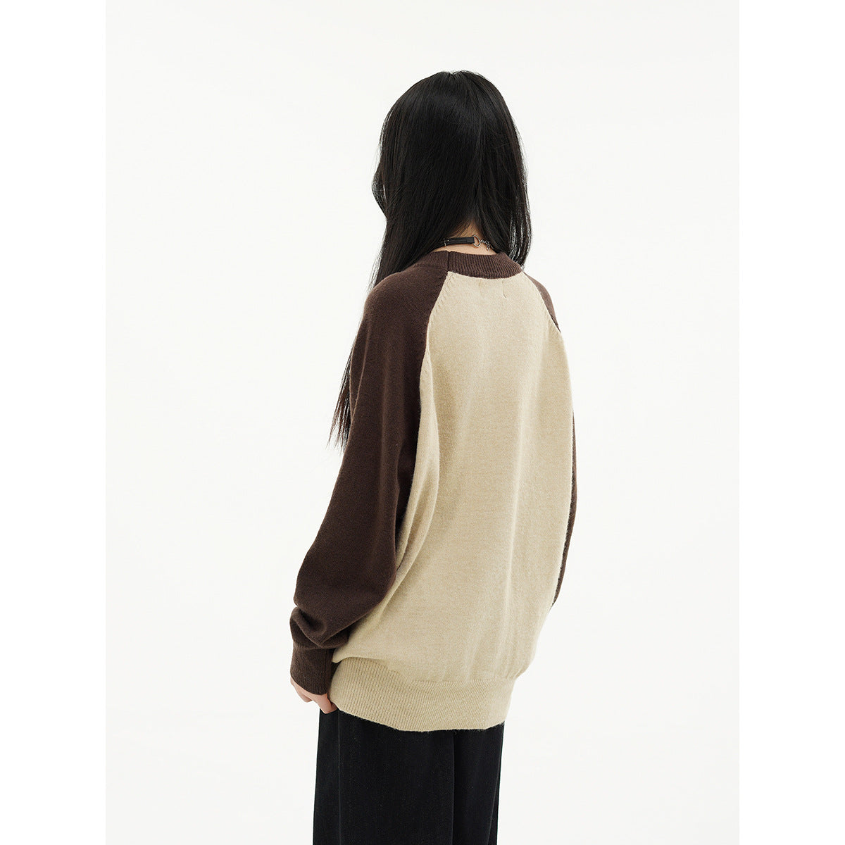Back view of a model wearing a cream raglan sweater with dark brown sleeves and ribbed cuffs and hem.