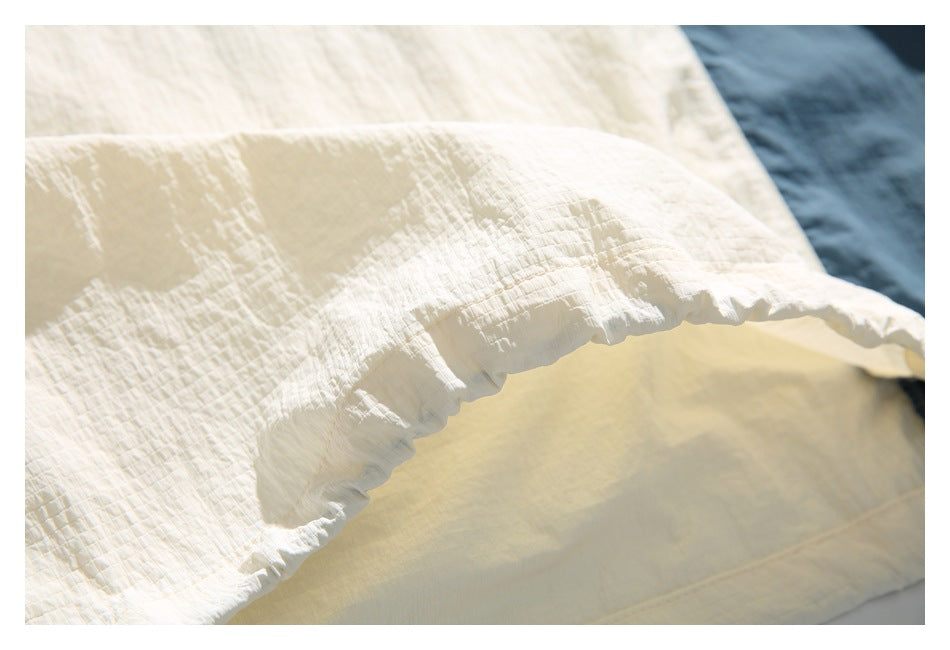 Close-up of a cream garment's crinkled fabric and gathered edge, with blue fabric in the background.