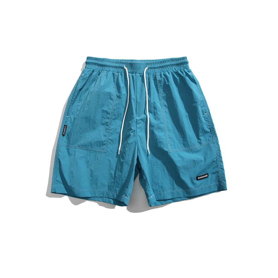 Blue shorts shown from the front, with an elastic drawstring waist, white cords, and two large pockets.