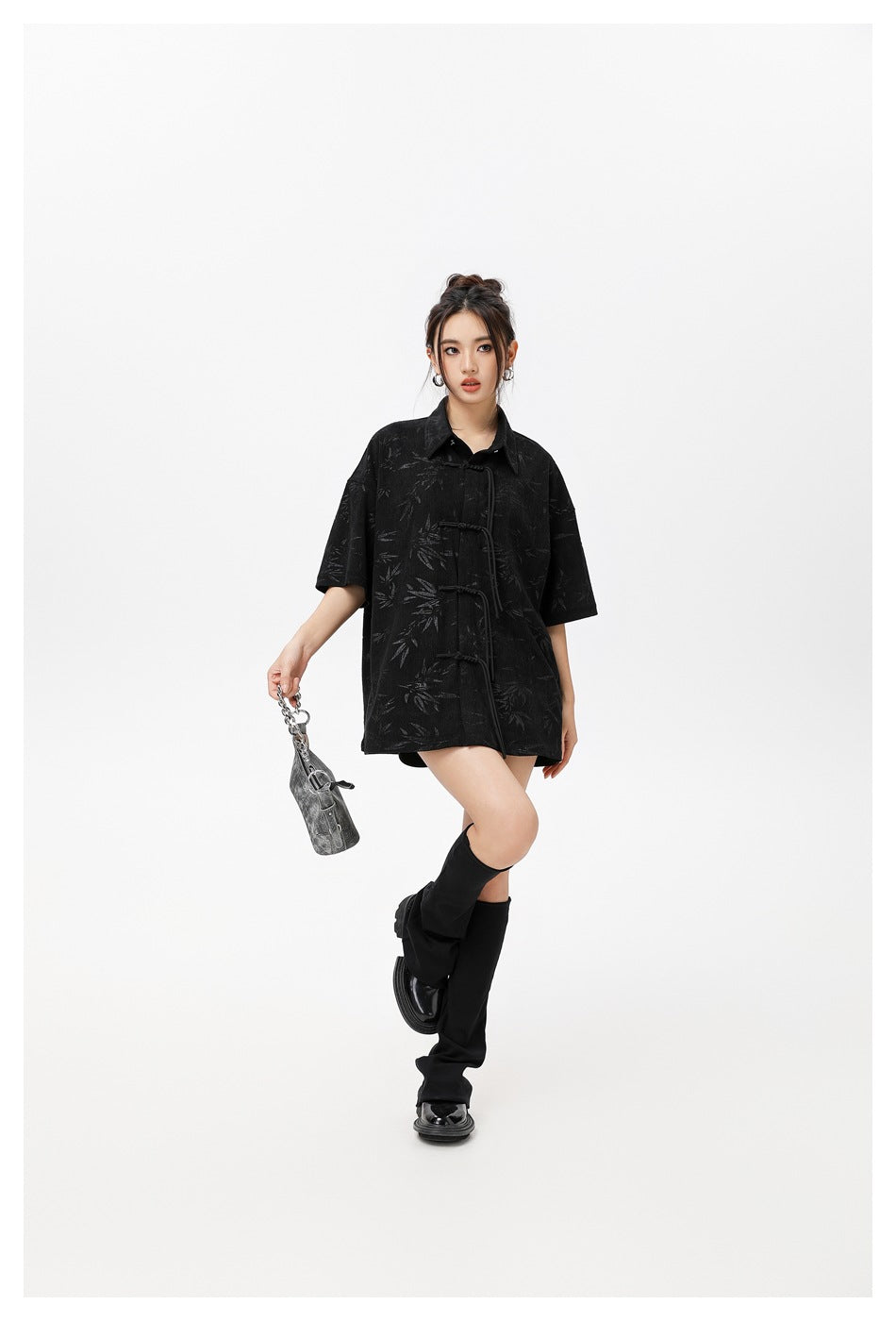 Full-length view of a model in an oversized black patterned shirt with short sleeves and frog closures.