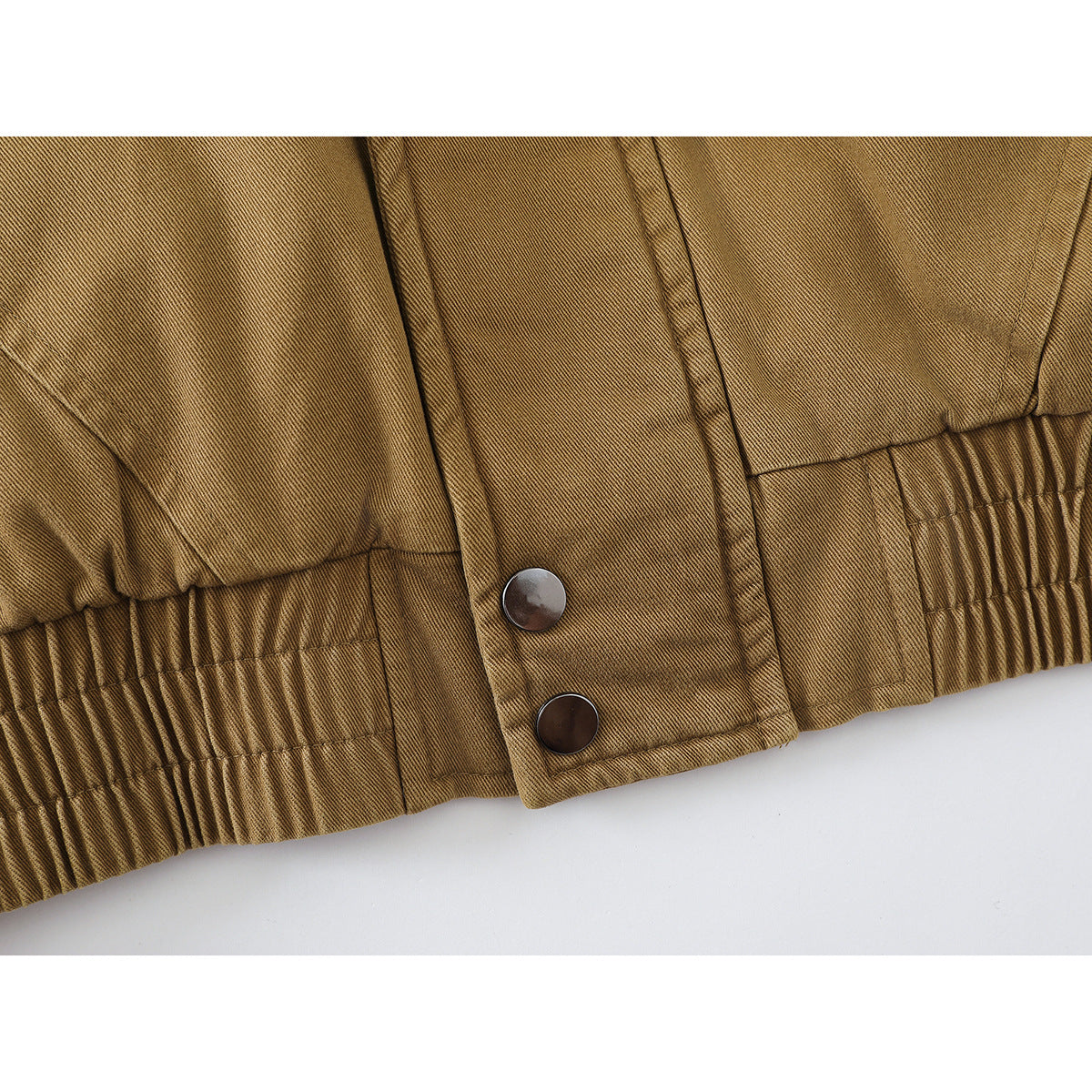 Close-up of a tan jacket hem with elastic gathering and two snap fasteners.