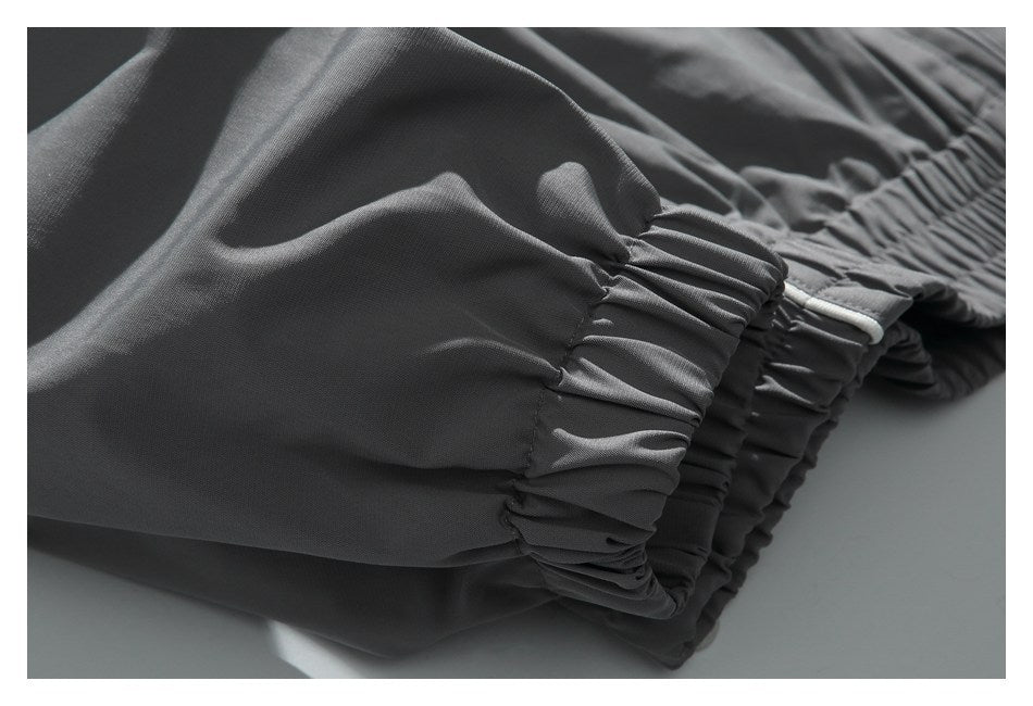 Close-up of charcoal pants gathered at an elastic ankle cuff, with a narrow light trim.