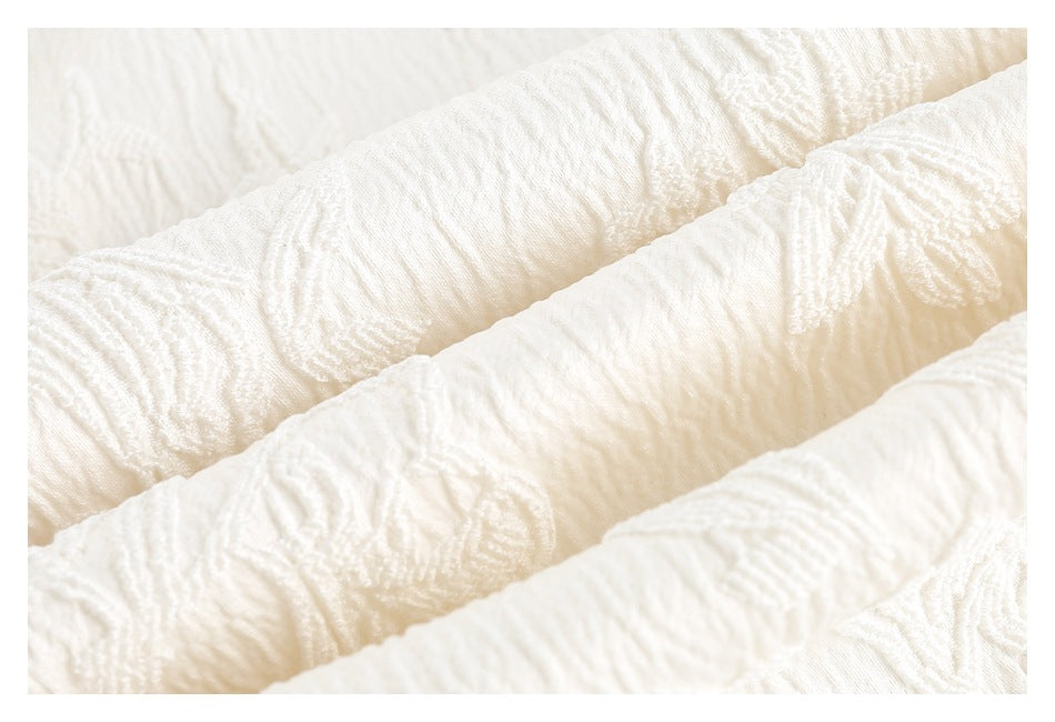 Extreme close-up of white fabric showing raised floral motifs and a rippled texture.