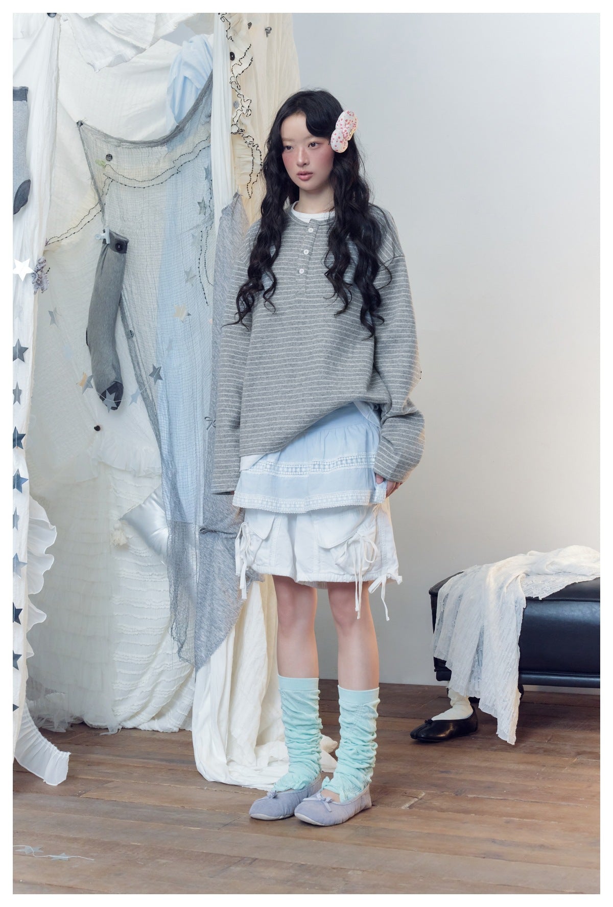 Model in loose gray striped Henley top layered over a white underlayer with a blue skirt and white shorts