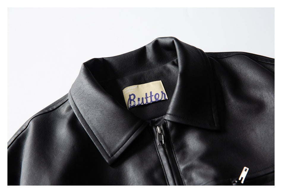 Close-up of a black jacket's pointed collar, center zipper, and cream Butter neck label.