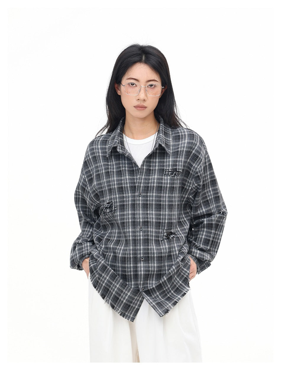 Model wearing an oversized charcoal gray plaid button-up shirt with distressed accents, over a white top and trousers.