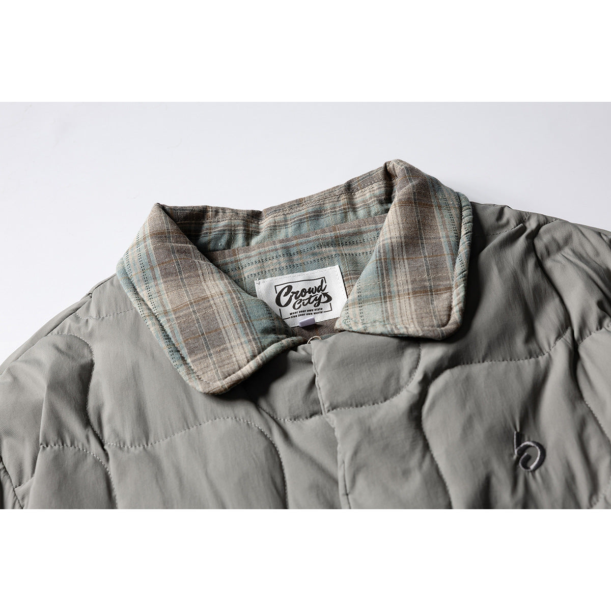 Close-up of a gray quilted jacket with a muted plaid collar and a small chest emblem.