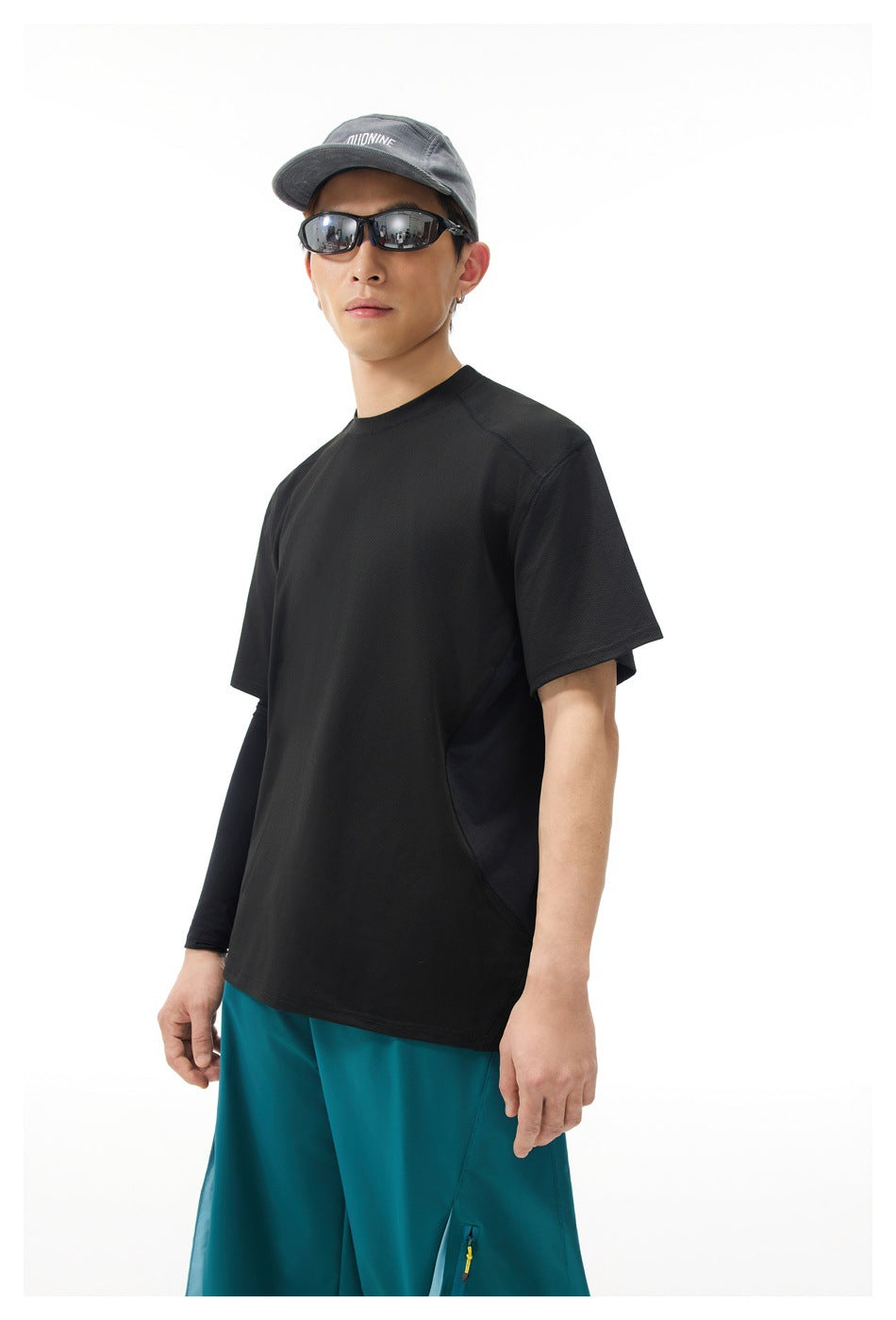 Model wearing a black short-sleeve shirt with teal pants, shown from the front at an angle.