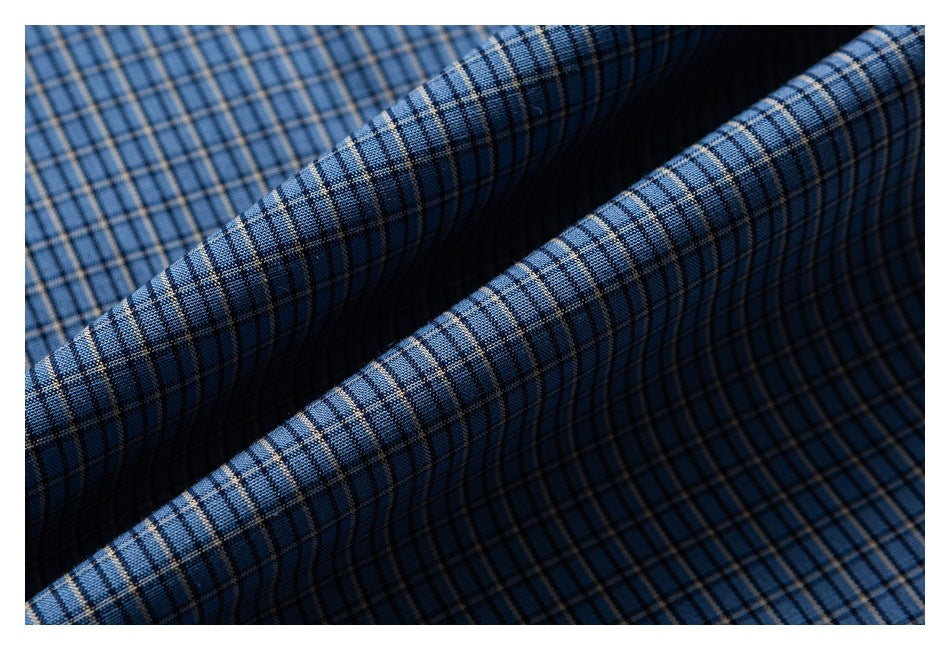 Close-up of blue fabric with a fine black and tan plaid pattern, folded into soft ridges.