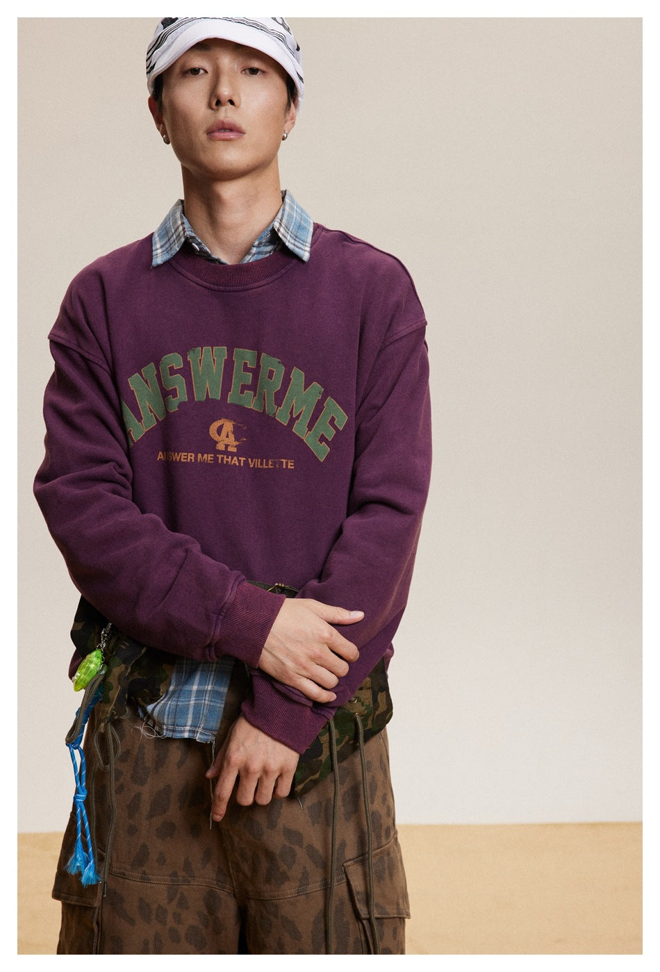 Model in a burgundy graphic crewneck sweatshirt over a blue plaid shirt, shown from the waist up.