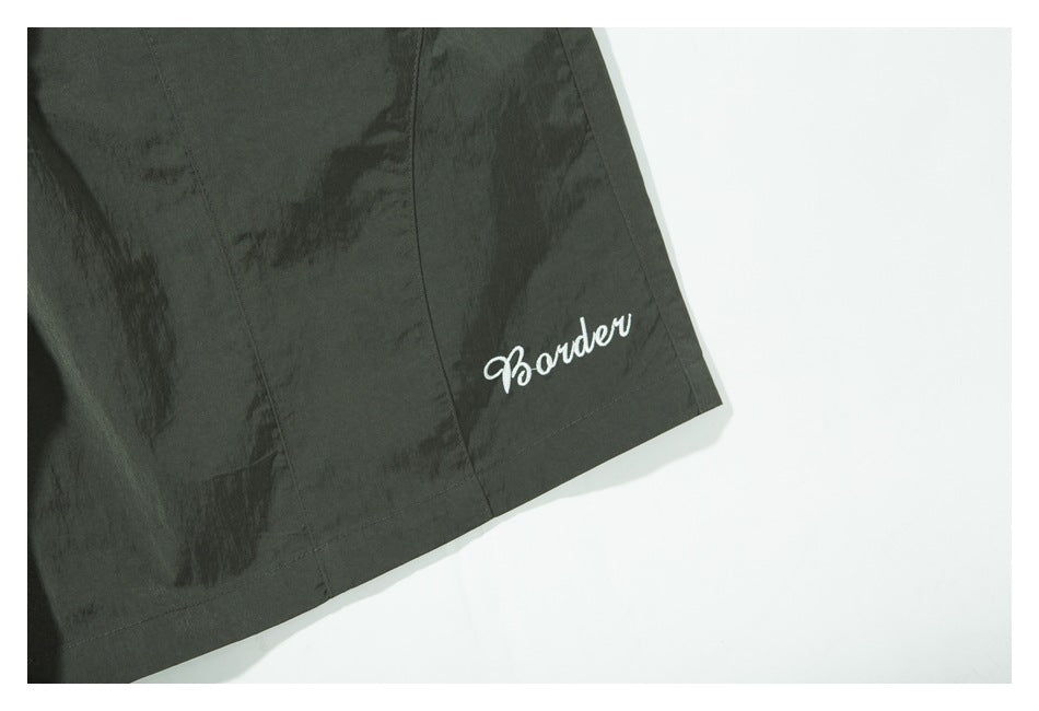 Close-up of the shorts' leg with white “Border” embroidery near the hem.