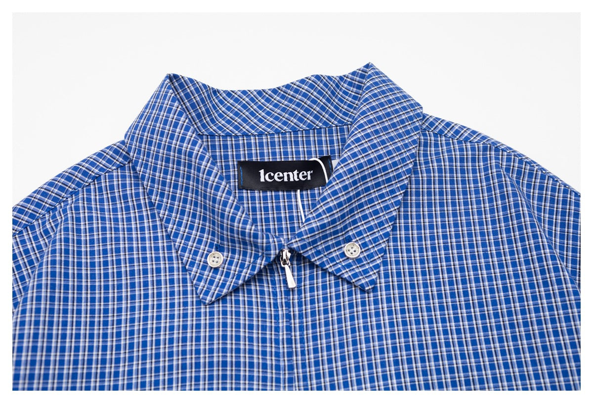 Close-up of a blue plaid shirt collar with button details, a center zipper, and a sewn black neck label.