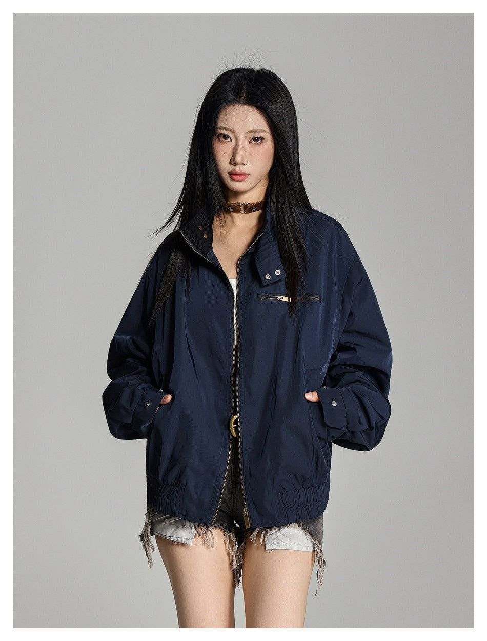 Model wearing a navy zip jacket with stand collar, hands in pockets, with a brown choker and frayed denim shorts