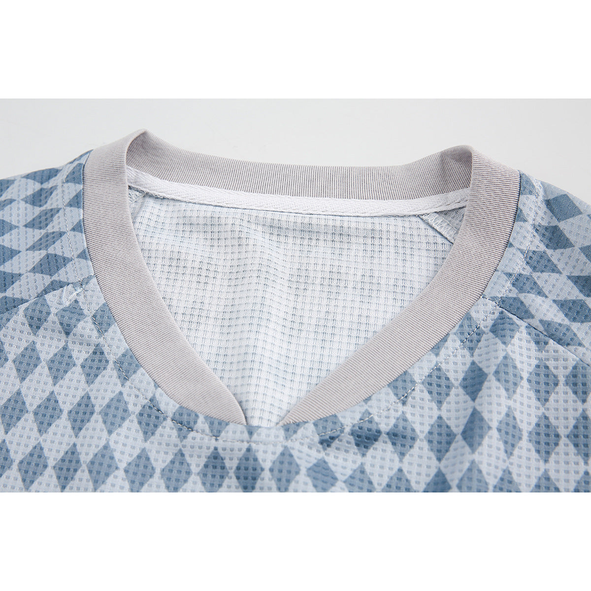 Close-up of a blue and gray diamond-patterned shirt, showing its V-neck ribbed trim and mesh-like inner panel.