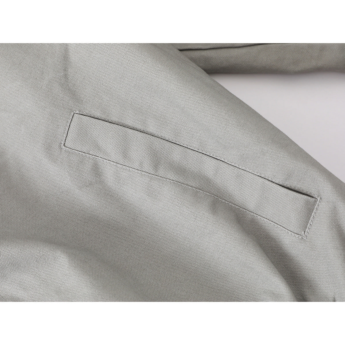 Close-up of a narrow welt pocket and stitching on light gray jacket fabric.