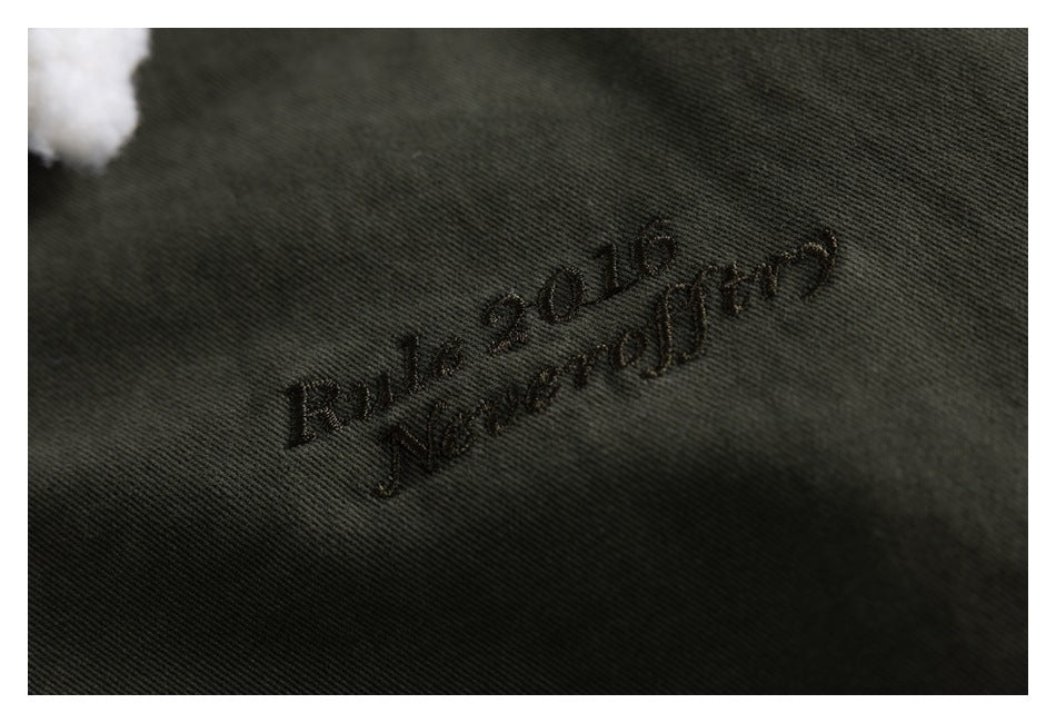 Close-up of dark tonal script embroidery on olive-gray jacket fabric.