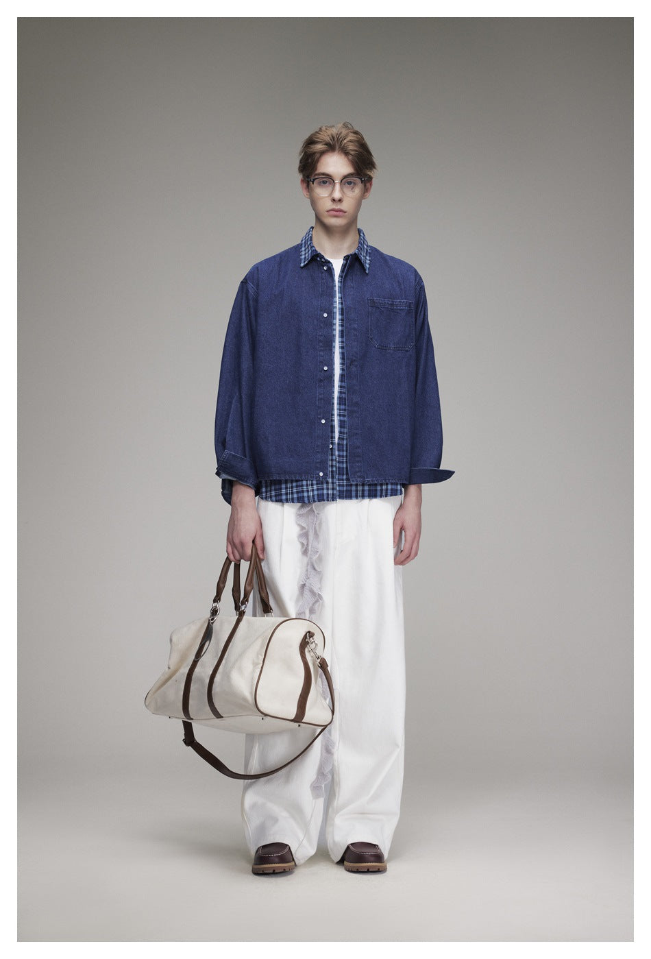 Front view of a model wearing a blue denim overshirt with plaid trim and white wide-leg trousers, carrying a cream bag.