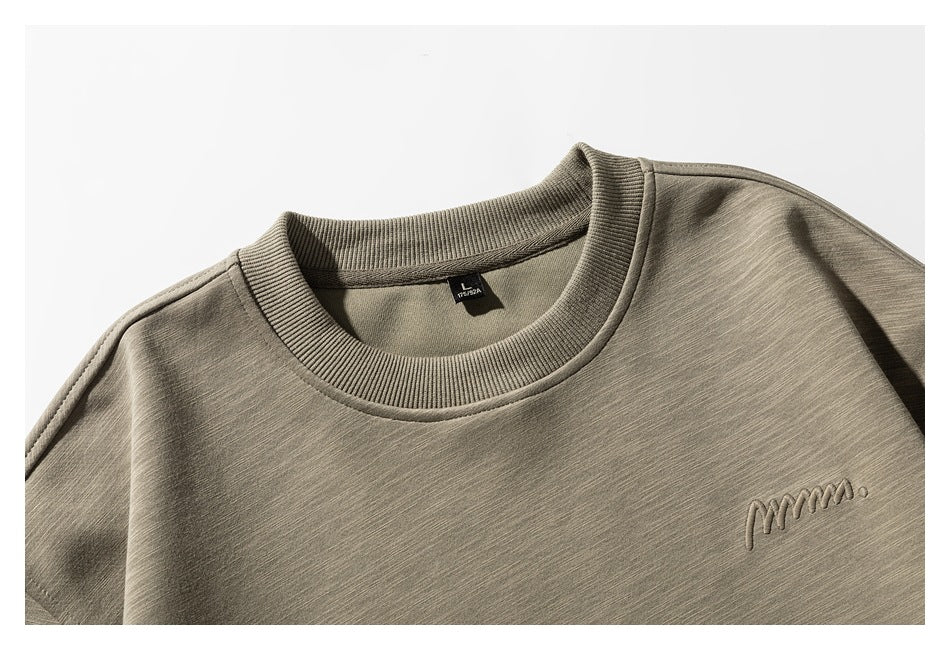 Close-up of an olive-gray crewneck sweatshirt front with ribbed neckline and small tonal embroidered chest script.