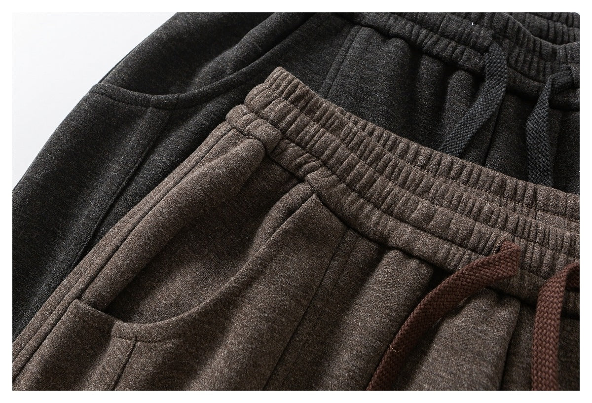 Close-up of dark charcoal and brown trousers layered together, showing elastic waistbands, pockets and drawstrings.