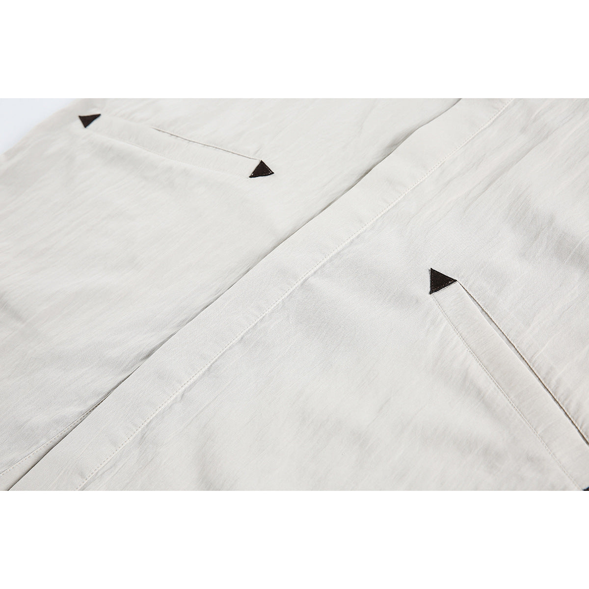 Close-up of a light beige shirt front with stitched placket and pocket openings edged with dark triangles.