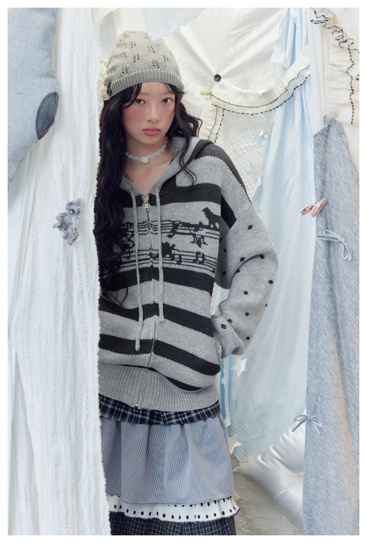 Model wearing a gray and black striped zip-up hooded sweater with animal motifs and dotted sleeves.