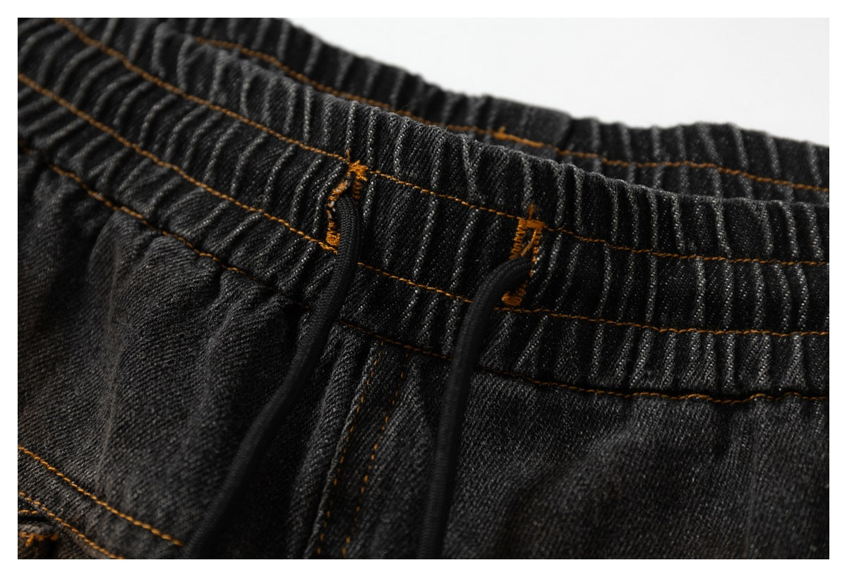 Close-up of charcoal-black pants with a gathered elastic waistband, black drawstrings, and ochre stitching.