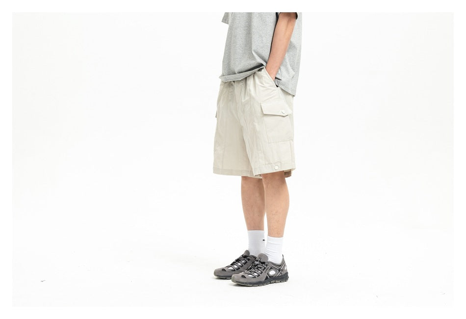Cropped side view of a model wearing ivory cargo shorts with a flap pocket and gray outdoor shoes.