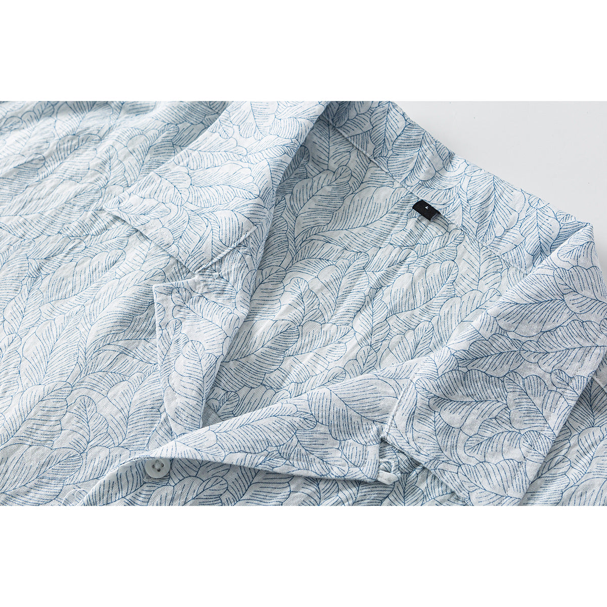Close-up of a pale blue and white leaf-print shirt showing its collar, placket, button, and small black tag.