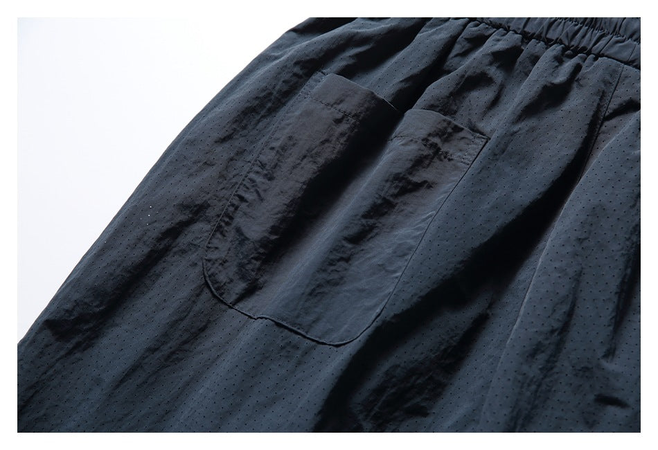 Close-up of a patch pocket and perforated fabric on black shorts.