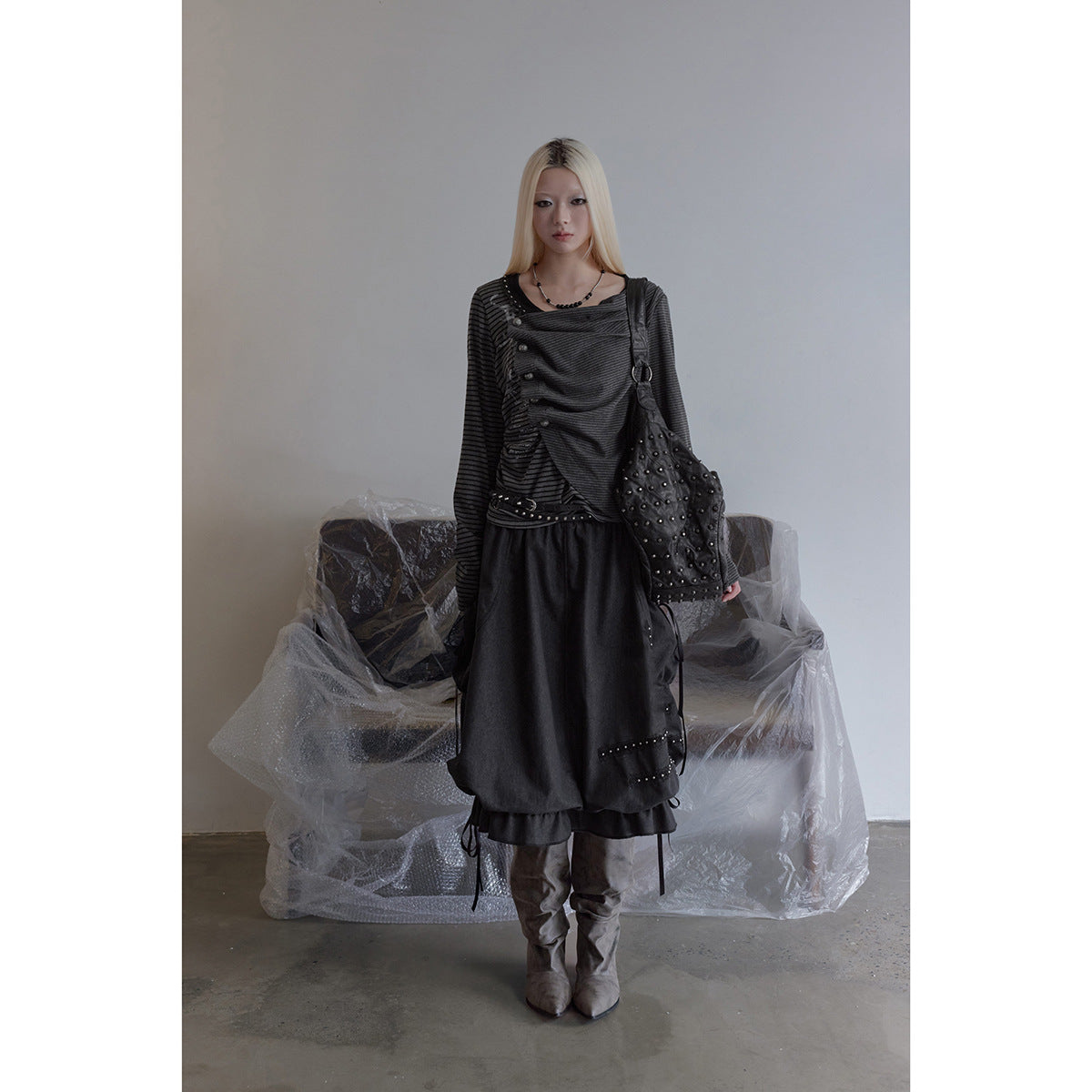 Model standing in a charcoal gathered skirt with a ruffled hem, studded trim, and side ties.
