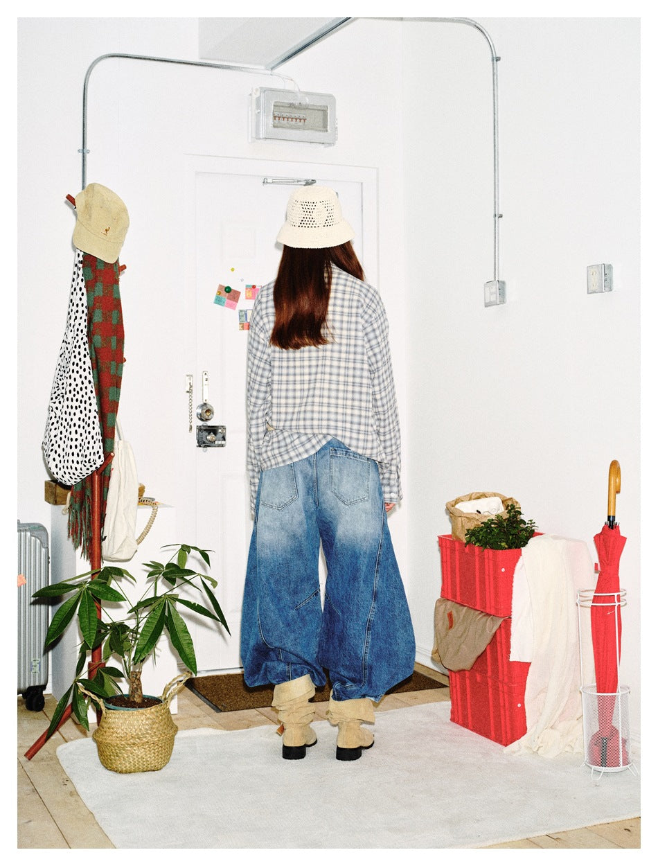 Rear view of a model wearing a gray-blue plaid shirt and loose blue jeans with large back pockets.