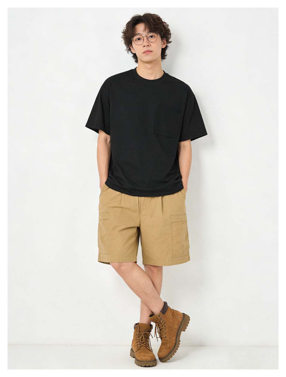 Man in black short-sleeve pocket T-shirt with khaki cargo shorts and tan boots, standing front view
