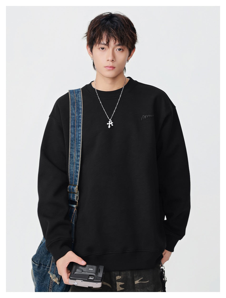Model wearing a black oversized crewneck sweatshirt with a small embroidered chest mark, holding a compact camera.