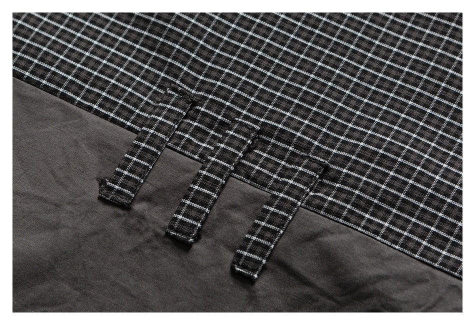 Close-up of a black checked shirt edge with three narrow fabric tabs and visible stitching.