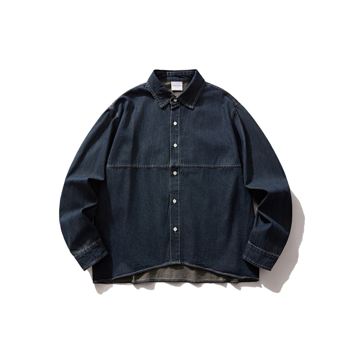 Dark blue washed denim button-front shirt flat lay with collar, chest seam, contrast stitching and curved hem