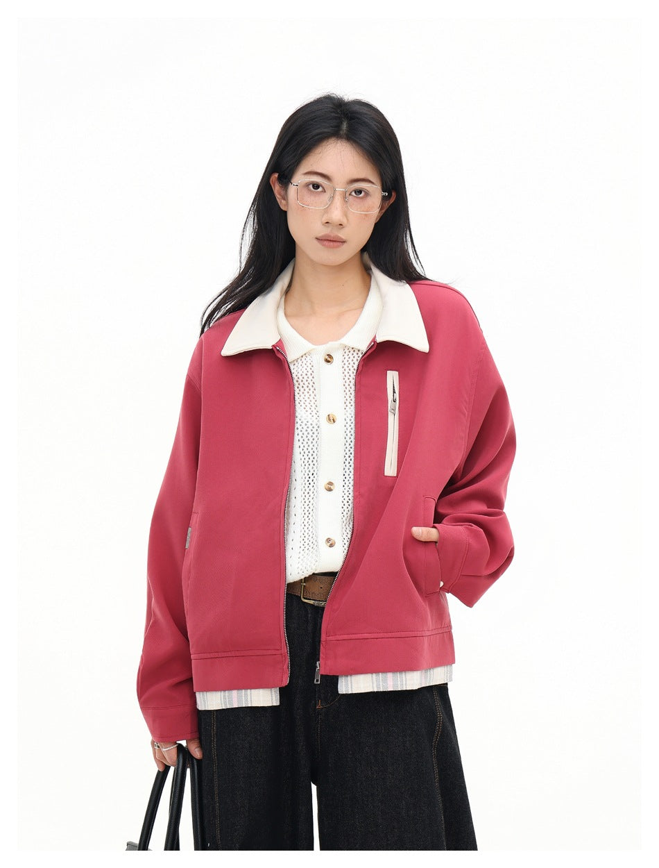 Close view of a person wearing a red collared zip jacket with cream collar and plaid-look hem over a white knit top